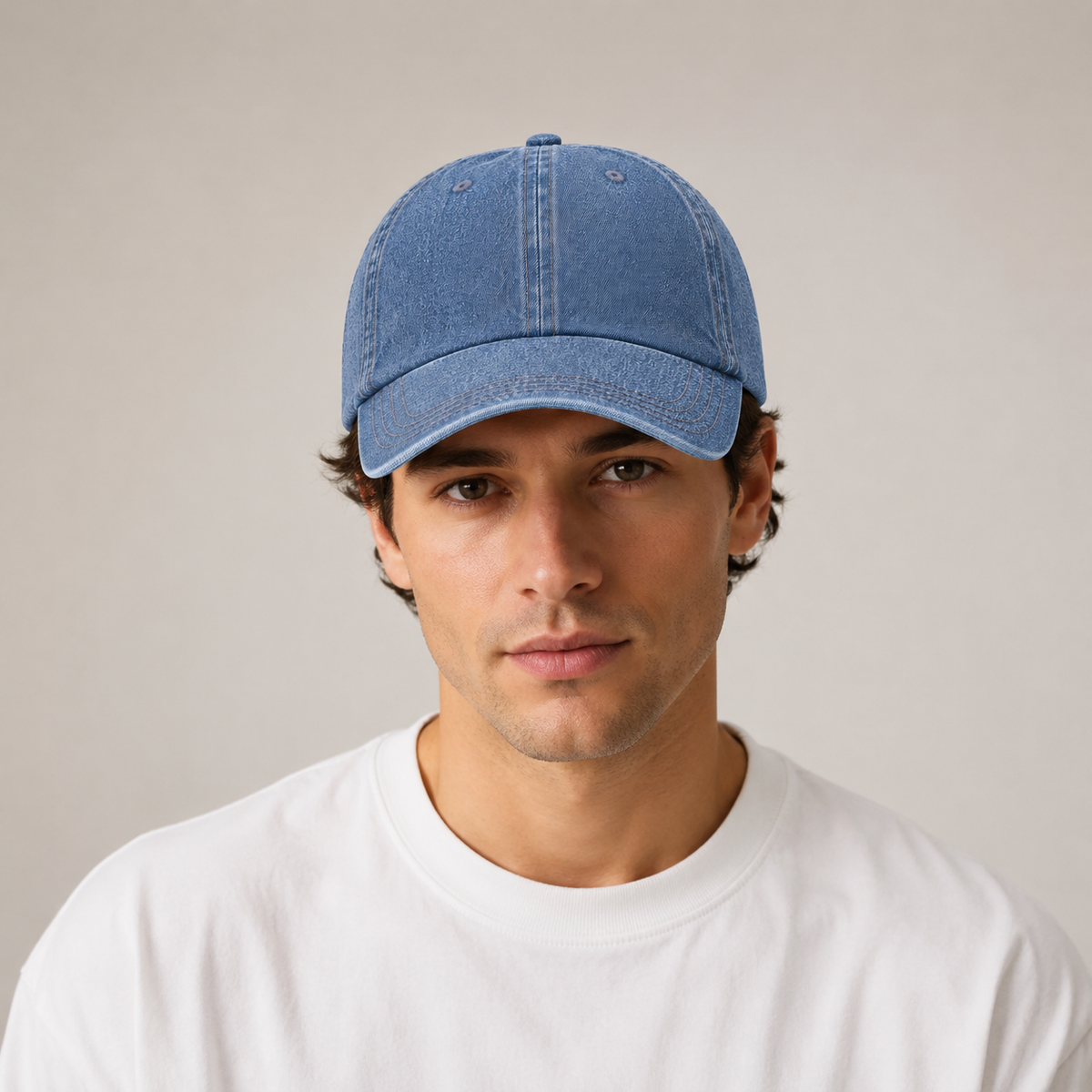 A man wearing a light blue washed denim baseball cap and a white crewneck t-shirt, photographed against a neutral light gray background.